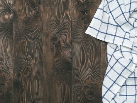 View from above on brown wooden table with linen kitchen towel or textile napkin. Blue tablecloth on dark brown wood tabletop. Copy space for text. Can use as mock up for design