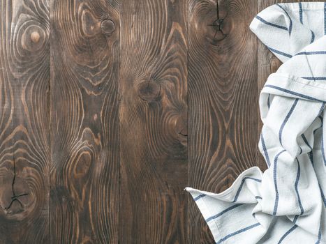 View from above on brown wooden table with linen kitchen towel or textile napkin. Blue tablecloth on dark brown wood tabletop. Copy space for text. Can use as mock up for design