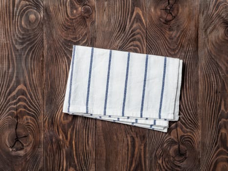 View from above on brown wooden table with linen kitchen towel or textile napkin. Blue folded tablecloth on dark brown wood tabletop. Copy space for text. Can use as mock up for design
