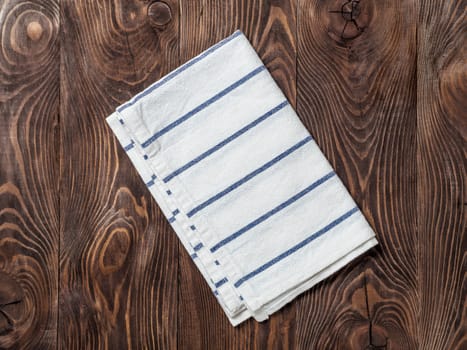 View from above on brown wooden table with linen kitchen towel or textile napkin. Blue folded tablecloth on dark brown wood tabletop. Copy space for text. Can use as mock up for design