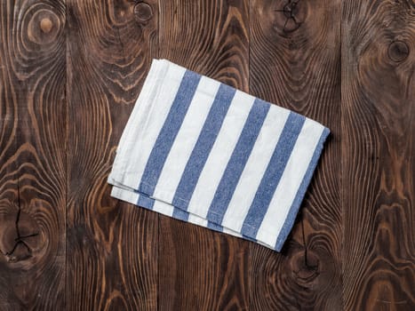 View from above on brown wooden table with linen kitchen towel or textile napkin. Blue folded tablecloth on dark brown wood tabletop. Copy space for text. Can use as mock up for design