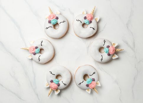 Unicorn donuts over white marble background. Trendy donut unicorn with white glaze in circle shape. Top view or flat lay. Copy space for text.