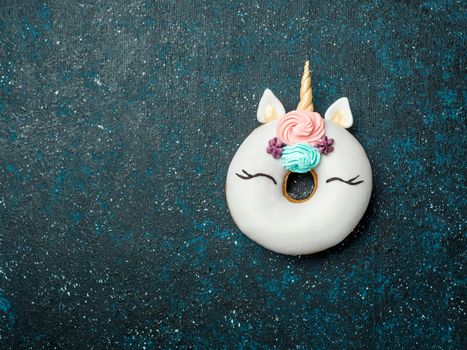 Unicorn donut over dark background. Trendy donut unicorn with white glaze. Top view or flat lay. Copy space for text.