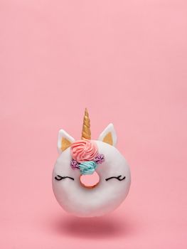 Unicorn donut hovers in air over pink background. Trendy donut unicorn with white glaze flying. Copy space for text. Vertical.