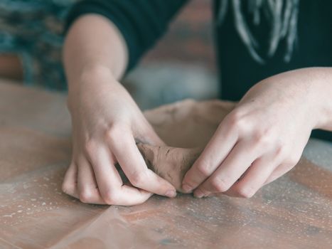 Female ceramist hands make trendy plate of brown clay. Close up view of fingers made fashion dessert flat plate on craft workshop.