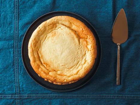 Plate with whole cheesecake pie on table with jeans tablecloth. Classic cheesecake flat lay or top view. Vertical.