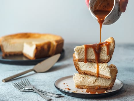 Caramel pouring on stack of three cheesekace pieces. Cheesecake with caramel on gray cement background. Copy space for text.