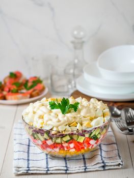 Large glass bowl with crab salad, corn, cucumber and rice at table. Layered crab sticks and corn salad. Traditiolnal mayonnaise salad for russian holiday feast, including new year. Vertical.Copy space