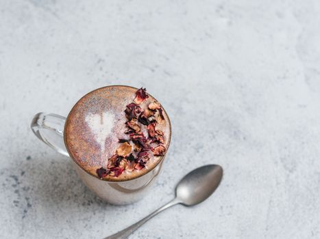 Trendy Coffee with edible glitter and dried rose petals. Cup of sparkly coffee or diamond cappuccino on gray table. Copy space for text. Top view or flat lay.