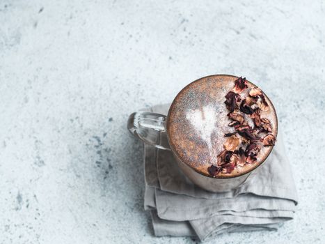 Trendy Coffee with edible glitter and dried rose petals. Cup of sparkly coffee or diamond cappuccino on gray table. Copy space for text. Top view or flat lay.