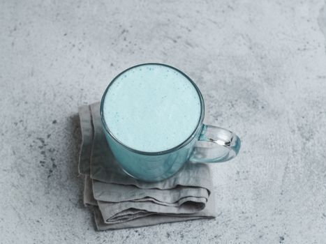 Trendy drink: Blue latte. Top view of hot butterfly pea latte or blue spirulina latte on gray cement textured background. Copy space for text. Top view or flat lay.