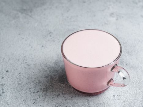 Trendy drink: pink latte. Beetroot or raspberries cappuccino or latte in glass cup on gray cement background. Copy space for text.