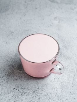 Trendy drink: pink latte. Beetroot or raspberry cappuccino or latte in glass cup on gray cement background. Copy space for text. Vertical.