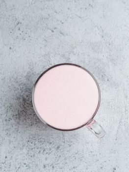 Trendy drink: pink latte. Beetroot or raspberry cappuccino or latte in glass cup on gray cement background. Copy space for text. Vertical. Top view or flat lay.