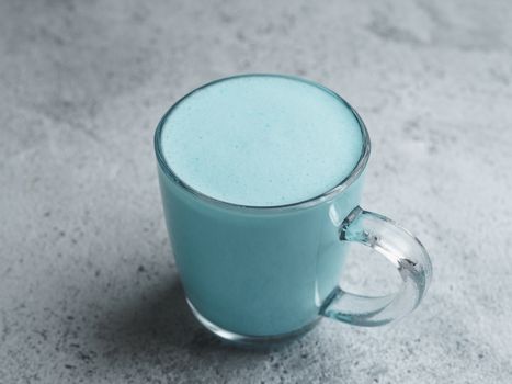 Trendy drink: Blue latte. Top view of hot butterfly pea latte or blue spirulina latte on gray cement textured background. Copy space for text.