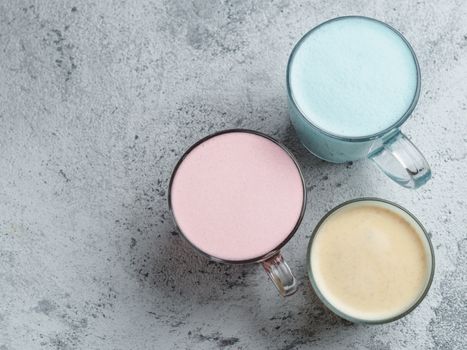 Trendy drinks: Blue, yellow and pink latte. Top view of hot butterfly pea or blue spirulina latte, yellow or gold turmeric latte and pink beetroot latte on gray cement background. Copy space for text