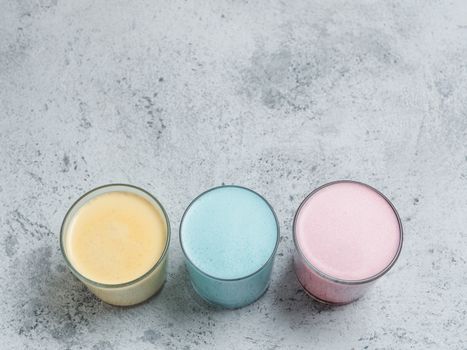 Trendy drinks: Blue, yellow and pink latte. Top view of hot butterfly pea or blue spirulina latte, yellow or gold turmeric latte and pink beetroot latte on gray cement background. Copy space for text