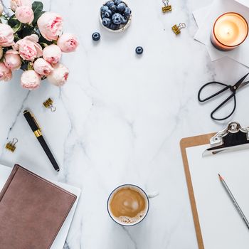 Top view of female home office with copy space in center. Clipboard, flowers, scented candle on white marble. Feminine home office mock up with copy space for text or design. Flat lay