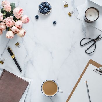 Top view of female home office with copy space in center. Clipboard, flowers, scented candle on white marble. Feminine home office mock up with copy space for text or design. Flat lay