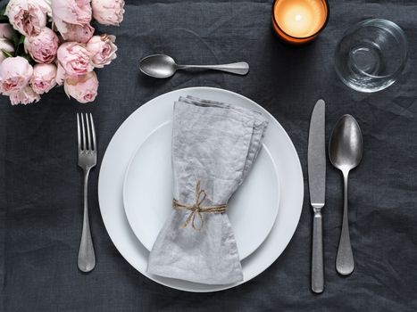 Beautiful table setting with pink spray roses and candle on gray linen tablecloth. Festive table setting for wedding dinner with gray linen napkin on plate. Holiday dinner at home, with white plates