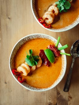 Tom yam kong ready-to-eat. Tom yum soup with shrimps on wooden table. Popular spicy Thai dish Tom Yam top view. Thailand food and Thai cuisine. Vertical. Natural day light