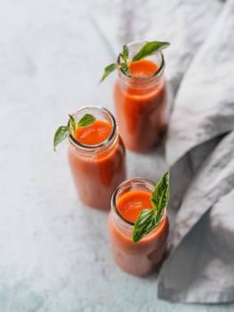 Delicious gaspacho soup in glass bottles. Traditional spanish cold soup puree gaspacho or gazpacho on gray cement background. View from above or top view or flat lay. Vertical.
