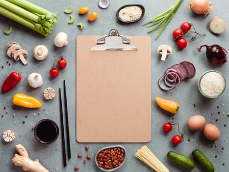 Asian ingredients and empty clipboard. Various of Chinese cooking ingredients and chopsticks on gray stone background. Asian food recipes concept. Copy space for text. Top view or flat lay.