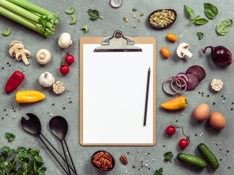 Food ingredients, salad serving utensils and clipboard with white paper sheet. Various of vegetarian cooking ingredients on gray background.Recipe book concept.Copy space for text.Top view or flat lay