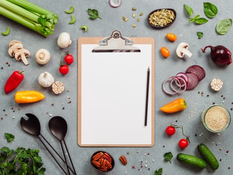 Food ingredients, salad serving utensils and clipboard with white paper sheet. Various of vegetarian cooking ingredients on gray background.Recipe book concept.Copy space for text.Top view or flat lay