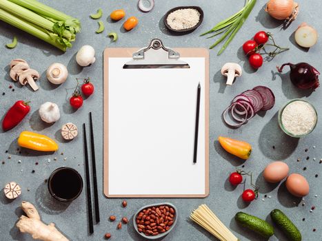 Asian ingredients and clipboard with white paper sheet. Various of Chinese cooking ingredients and chopsticks on gray stone background. Asian food concept. Copy space for text. Top view or flat lay.