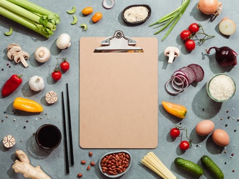 Asian ingredients and empty clipboard. Various of Chinese cooking ingredients and chopsticks on gray stone background. Asian food recipes concept. Copy space for text. Top view or flat lay.