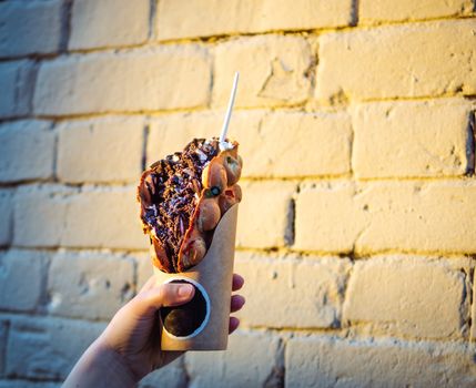 Hong Kong waffles in female hand on brick wall background. Delicious bubble waffle with chocolate biscuit cookies and chocolate syrup in beautiful sunset light. Copy space for text.