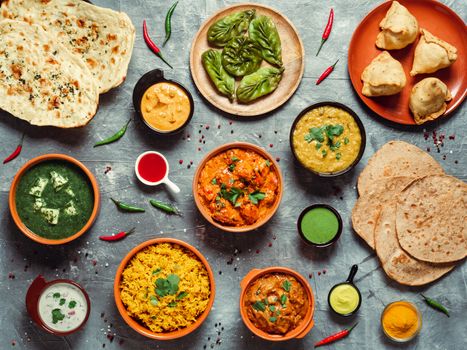 Indian cuisine dishes: tikka masala, dal, paneer, samosa, chapati, chutney, spices. Indian food on gray background. Assortment indian meal top view or flat lay.