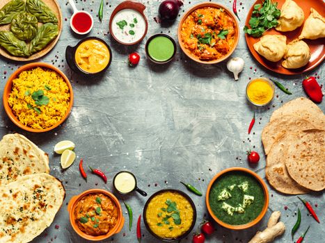 Indian cuisine dishes: tikka masala, dal, paneer, samosa, chapati, chutney, spices. Indian food on gray background. Assortment indian meal with copy space for text in center. Top view or flat lay.