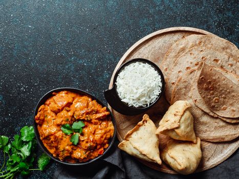 Indian cuisine dishes: tikka masala, rice, samosa, chapati,. Indian food on dark background with copy space. Assortment indian meal top view or flat lay.