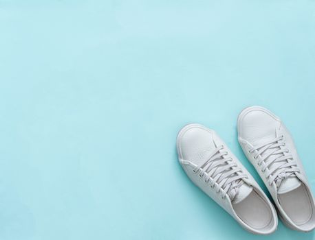 White leather sneakers on blue background. Pair of fashion trendy white sport shoes or sneakers with copy space for text or design. Overhead shot of new white sneakers. Top view or flat lay.