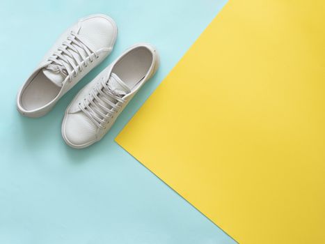 White leather sneakers on blue and yellow background. Pair of fashion trendy white sport shoes or sneakers with copy space for text on colorful background. Overhead shot of new white sneakers.Flat lay