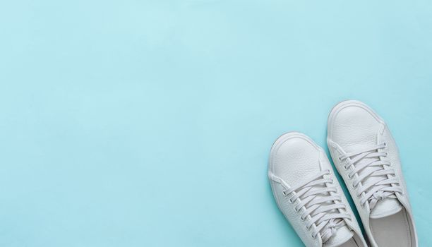 White leather sneakers on blue background. Pair of fashion trendy white sport shoes or sneakers with copy space for text or design. Overhead shot of new white sneakers. Top view or flat lay. Banner