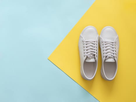 White leather sneakers on blue and yellow background. Pair of fashion trendy white sport shoes or sneakers with copy space for text on colorful background. Overhead shot of new white sneakers.Flat lay