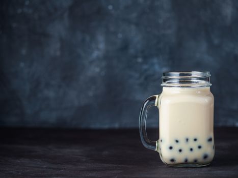 Homemade Milk Bubble Tea with Tapioca Pearls balls. Popular Taiwan bubble tea in glass mason jar with copy space for text. Bubble tea on dark background.