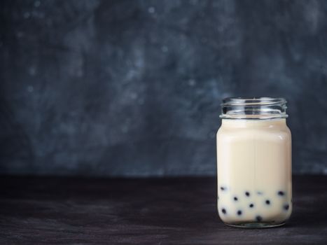 Homemade Milk Bubble Tea with Tapioca Pearls balls. Popular Taiwan bubble tea in glass mason jar with copy space for text. Bubble tea on dark background.