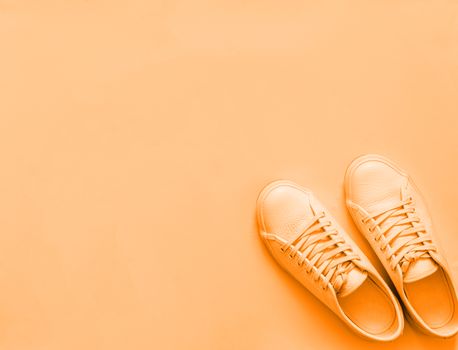 Orange leather sneakers on pastel orange background, monochrome. Pair of orange sport shoes with copy space for text or design. Top view or flat lay