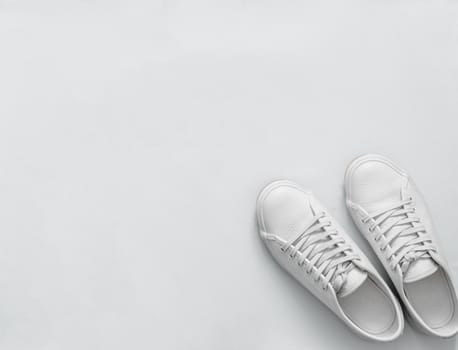 White leather sneakers on white background. Pair of fashion trendy white sport shoes or sneakers with copy space for text or design. Overhead shot of new white sneakers,monochrome.Top view or flat lay