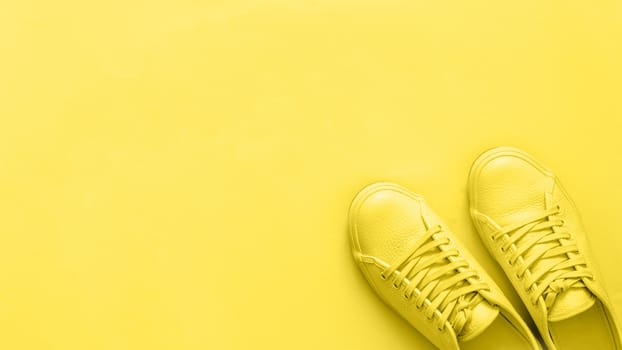 Yellow leather sneakers on yellow background. Pair of yellow sport shoes or sneakers with copy space for text or design. Overhead shot of new yellow sneakers, monochrome. Top view or flat lay