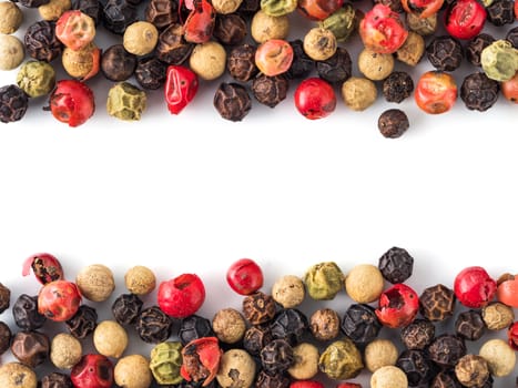 Mixed peppercorns background with white copy space in center. Food background with peppercorns. Different colored peppercorns pattern on white background, top view or flat lay