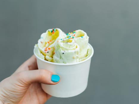 Rolled ice cream in cone cup in woman hand. Woman holds cone cup with thai style kiwi banana rolled ice cream. Outdoor. Natural daylight Copy space for text or design.