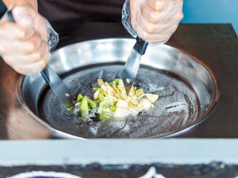 Making rolled ice cream. Man hands making kiwi and banana Thay style natural ice cream