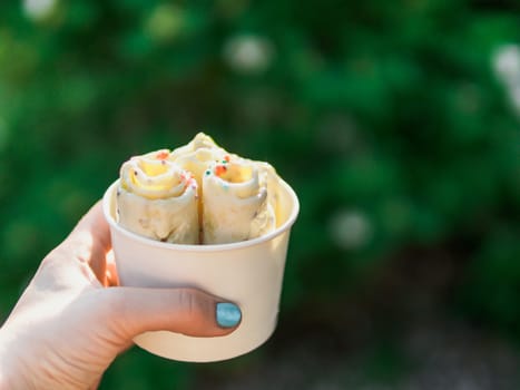 Rolled ice cream in cone cup in woman hand. Woman holds cone cup with thai style kiwi banana rolled ice cream. Outdoor. Natural daylight Copy space for text or design.