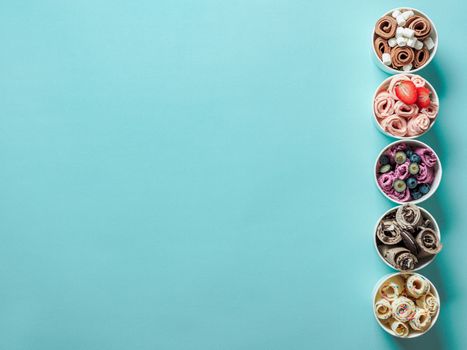 Rolled ice creams in paper cone cups on blue background. Different iced rolls, top view or flat lay. Thai style rolled ice cream with copy space for text or design