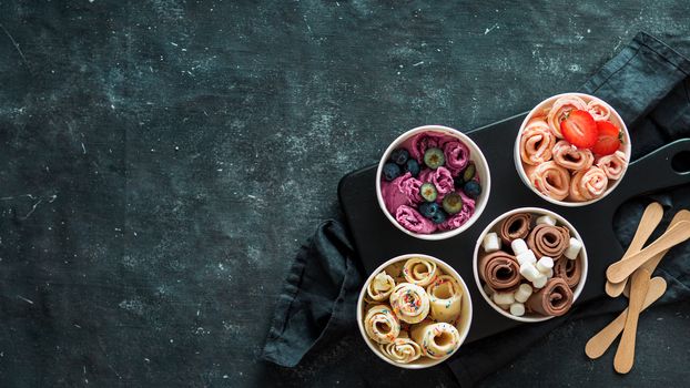 Rolled ice cream in cone cups on dark background. Different iced rolls top view or flat lay. Thai style rolled ice cream with copy space in center for text or design. Banner